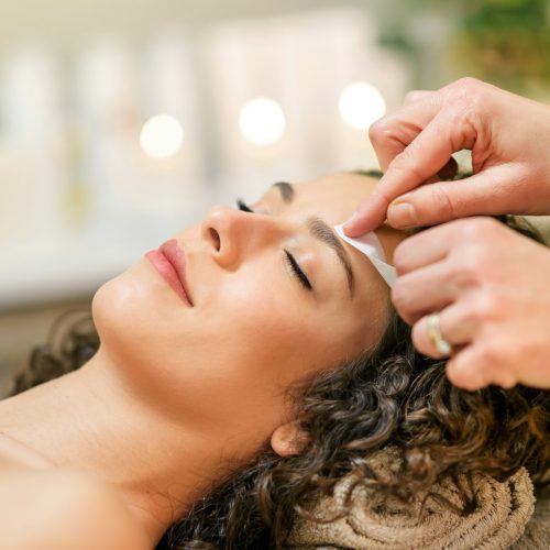 Master waxing eyebrow of relaxed client in beauty studio